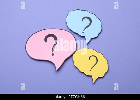 Different paper speech bubbles with question marks on violet background, flat lay Stock Photo
