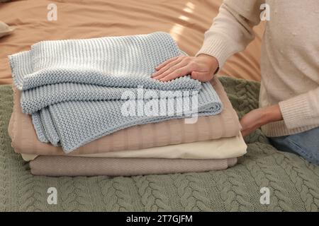 Woman with stack of different folded blankets on bed, closeup. Home textile Stock Photo