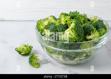 Glass bowl of fresh raw organic broccoli close-up on a marble kitchen table in a light background with a copy space Stock Photo