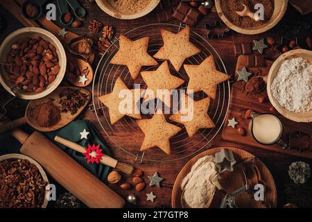 Baked Christmas biscuits on a cake rack, baking ingredients, Christmas decorations, flour, sugar, almonds, nuts, cinnamon, cookie cutters Stock Photo