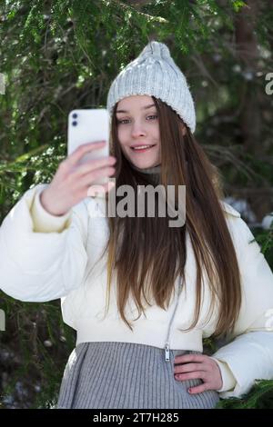 Smiling brunette teen girl using smartphone making video selfie to capturing moments from forest. Happiness teenager with long hair, without make-up Stock Photo