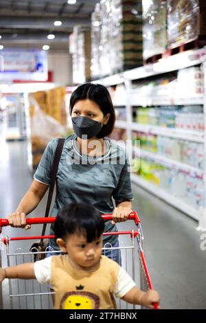 Mother pushing shopping cart with her infant baby boy child down department aisle in supermarket grocery store. Mother And Son At The Supermarket. Sho Stock Photo