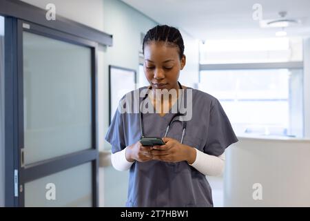 African american female doctor using smartphone in hospital corridor Stock Photo