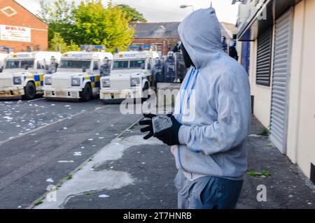 Rioter with his face covered about to throw brick at police landrovers Stock Photo