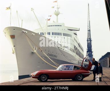 1966 newly launched Jaguar E-type Series 1 2+2 next to luxury ocean liner SS Canberra at Southampton Docks with family of four and lady in driving sea Stock Photo
