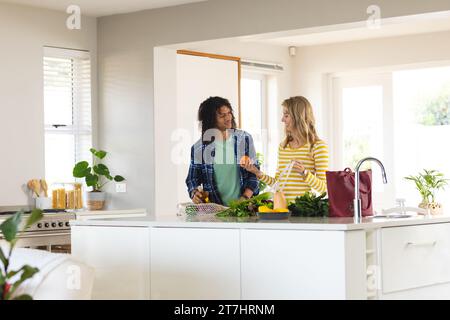 Happy diverse couple unpacking grocery shopping and smiling in sunny kitchen Stock Photo