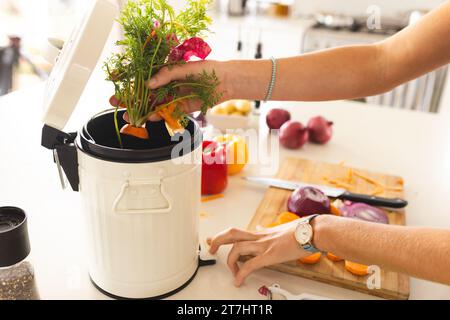 Hands of blonde caucasian woman composting vegetable waste in sunny kitchen at home Stock Photo