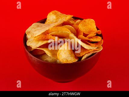 Potato chips in clay bowl isolated on red background. side view Stock Photo