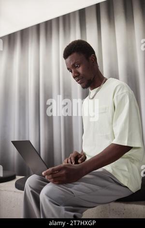 Vertical portrait of young Black man using laptop in minimal office lounge Stock Photo