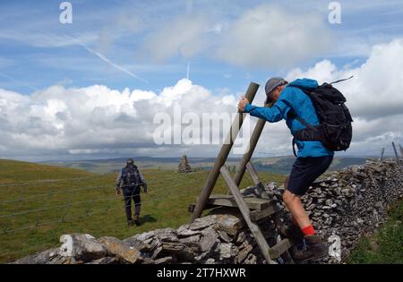 Elderly Man Climbing Wooden Ladder Stile over Dry Stone Wall to the Summit Cairn of Addlebrough in Wensleydale, Yorkshire Dales, England, UK. Stock Photo