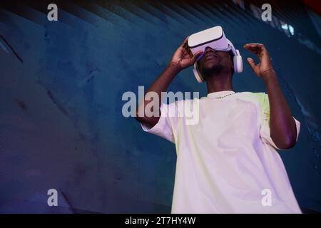 Futuristic low angle portrait of young Black man wearing VR headset against concrete wall, copy space Stock Photo
