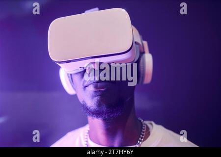 Front view closeup portrait of young African American man wearing VR headset in neon light entering cyberspace, copy space Stock Photo