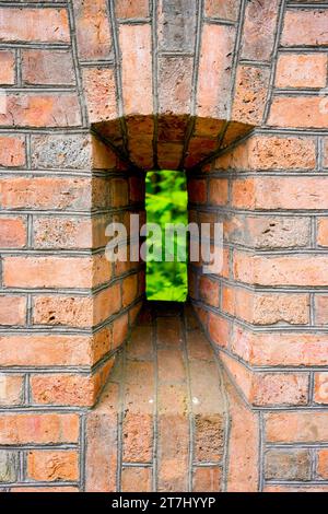 Embrasure on an old brick wall with a view of the greenery. Stock Photo