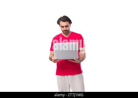 young black-haired man dressed in a red corporate t-shirt uses a laptop Stock Photo