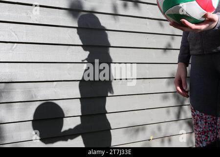 Teenage girl holds volleyball with her shadow on wall Stock Photo