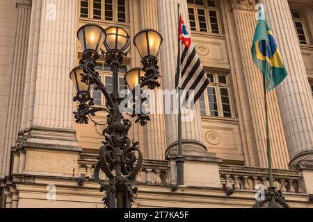 Old lamp lit with the facade of the Santos City Hall building in the background. Flags of the State of São Paulo and Brazil. Stock Photo