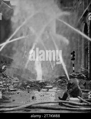 A fireman in action spraying water on a burning building in London, England following overnight air raids during the Second World War by the Luftwaffe in September 1940. Stock Photo