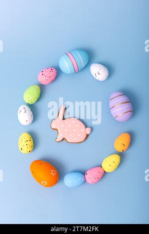 multicolored eggs and gingerbread in the form of a rabbit are scattered on a light blue background Stock Photo