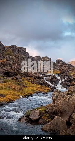 A picturesque landscape featuring a mountain stream winding through a rocky terrain and lush, green grassy hills in the background Stock Photo