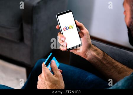 Ebay logo on phone screen held by a man with a credit card in the other hand. ROSARIO, ARGENTINA - NOVEMBER 15, 2023. Stock Photo