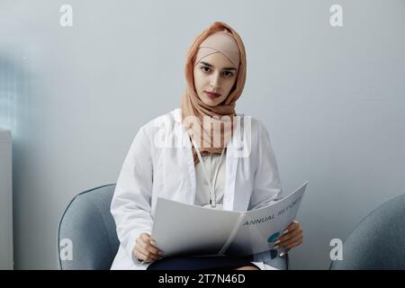 Minimal portrait of young Muslim woman as female doctor wearing headscarf in clinic and looking at camera, copy space Stock Photo