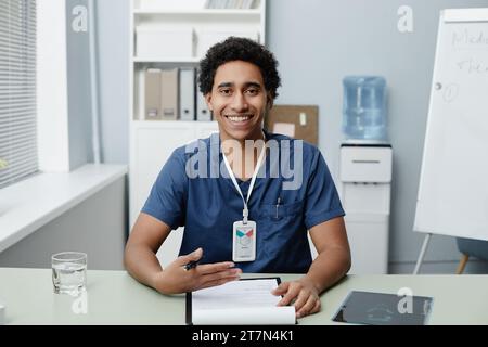 Portrait of smiling young Middle Eastern man as doctor speaking via video chat in clinic, copy space Stock Photo