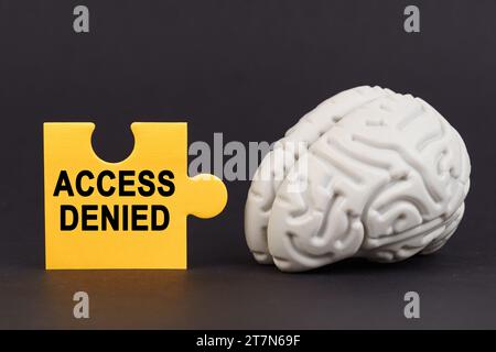 On a black surface there is a brain and a yellow puzzle with the inscription - access denied. Business and technology concept. Stock Photo