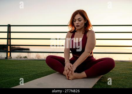 Curvy woman practices yoga by the sea, embracing serenity and mindfulness during a peaceful sunset. Stock Photo