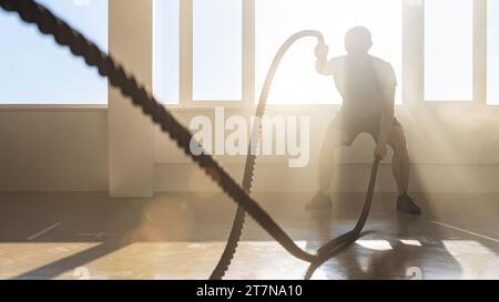 athletic men with battle rope in functional training fitness gym. crossfit exercises concept image Stock Photo