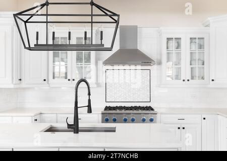 A kitchen detail with a black faucet and light fixture on the island, white cabinets, and a mosaic tile backsplash. No brands or logos. Stock Photo