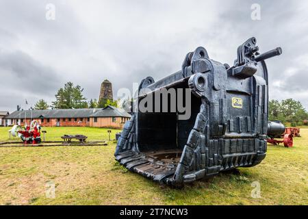 30-ton shovel from the open-cast iron ore mine. The Cliffs Shaft Mine Museum in the background. Silent witnesses of iron mining in the city of Ishpeming, United States Stock Photo