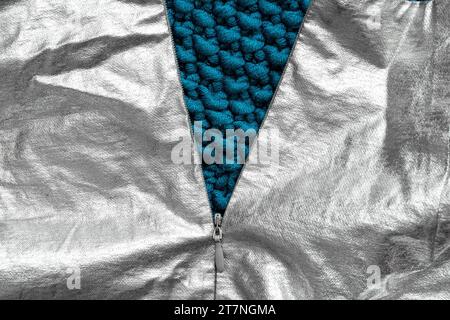 An unzipped zipper on a gray glossy fabric and a blue knitted fabric under the zipper as a background, fashion and trend Stock Photo