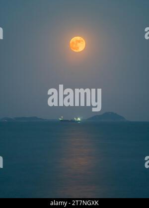 A stunning image of the night sky with a full moon hovering above a seascape of large rocks jutting out of the ocean's surface Stock Photo