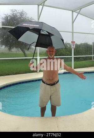 A man smiles holding an umbrella in a swimming pool in Orlando, Florida just before hurricane Irma. Stock Photo