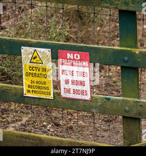 Warning CCTV in Operation and humorous No Trespassing signs on wooden fence, England, UK Stock Photo