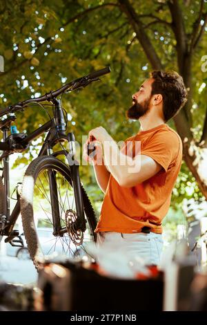Committed male cyclist using expert tools to repair and fix bike head-tube in home yard. Sports-loving caucasian man holding specialized equipment for mending bicycle outside as annual summer maintenance. Stock Photo
