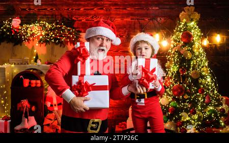 Christmas eve. Amazed Santa Claus and child with Christmas present. Family holidays and childhood. Little kid and bearded man in Santa Claus costume Stock Photo