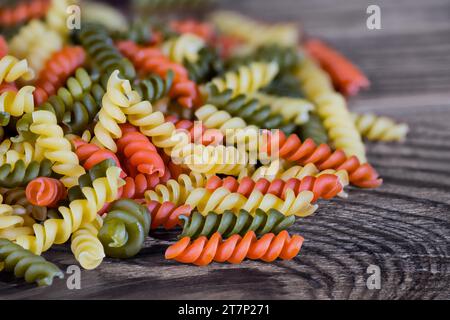 Heap of yellow, red or green helical shaped fusilli pasta on brown wooden background. Closeup a pile of raw colored rotini of tomato or spinach flavor. Stock Photo