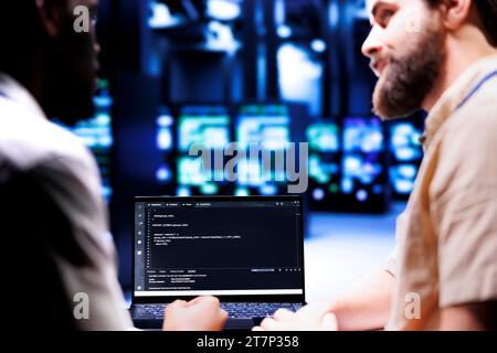 Colleagues updating server clusters, writing complex binary code scripts on laptop terminal. Admins using JavaScript, Java, and database programming to fortify security and safeguard data Stock Photo