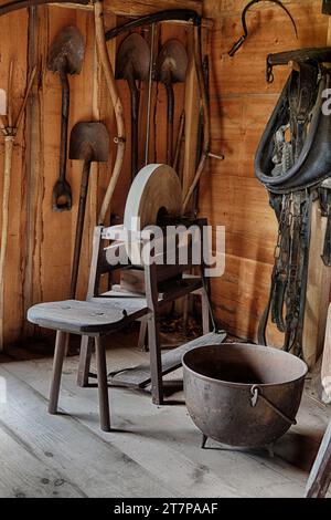 An antique treadle style grinding wheel displayed in a vintage reproduction barn with other tools from the 19th century. Stock Photo