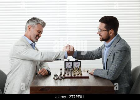 Men shaking their hands during chess tournament at table indoors Stock Photo