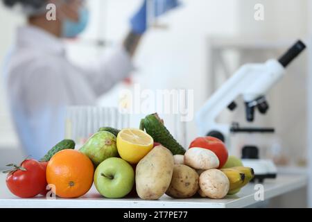Fresh vegetables, fruits on table and scientist proceeding quality control in laboratory Stock Photo