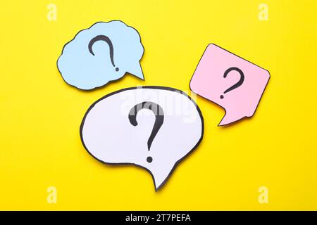 Different paper speech bubbles with question marks on yellow background, flat lay Stock Photo