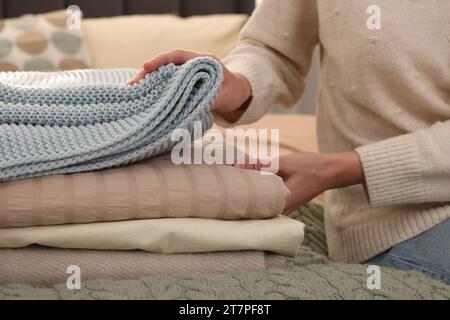 Woman with stack of different folded blankets on bed, closeup. Home textile Stock Photo