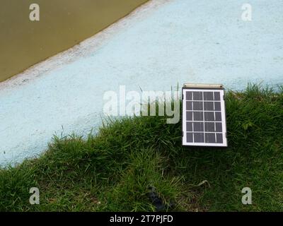 Small portable solar cell panel on the lawn at edge of pond, Clean energy for electricity generation in the home, Using alternative technology Stock Photo