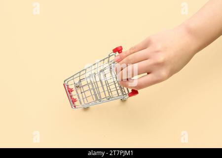 Female hand with red shopping cart on color background. Stock Photo