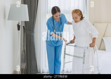 Asian elderly woman practice walking using walker aid with nurse care support step walk at homecare Stock Photo
