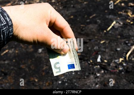 Coin and banknotes on black hot coal among ashes. Currency devaluated, finance and business concept Stock Photo