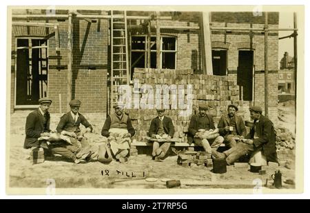 Original postcard of a relaxed group of bricklayers eating lunch during their lunchbreak outside a house which is still under construction, early 1920's dated from collars, there is a note on the front saying 12 till 1. Some good characters. U.K Stock Photo