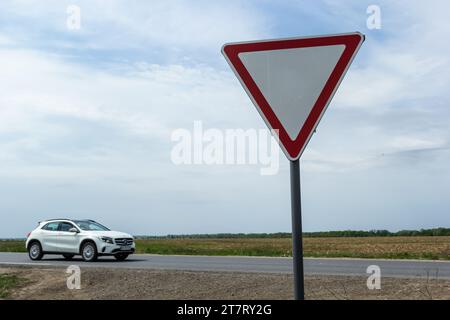 The sign Give way to the driver when exiting the highway at a rural intersection on the background of a passing car. Stock Photo